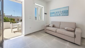 A room with a sofa, a painting, a window, and a view of the outside.