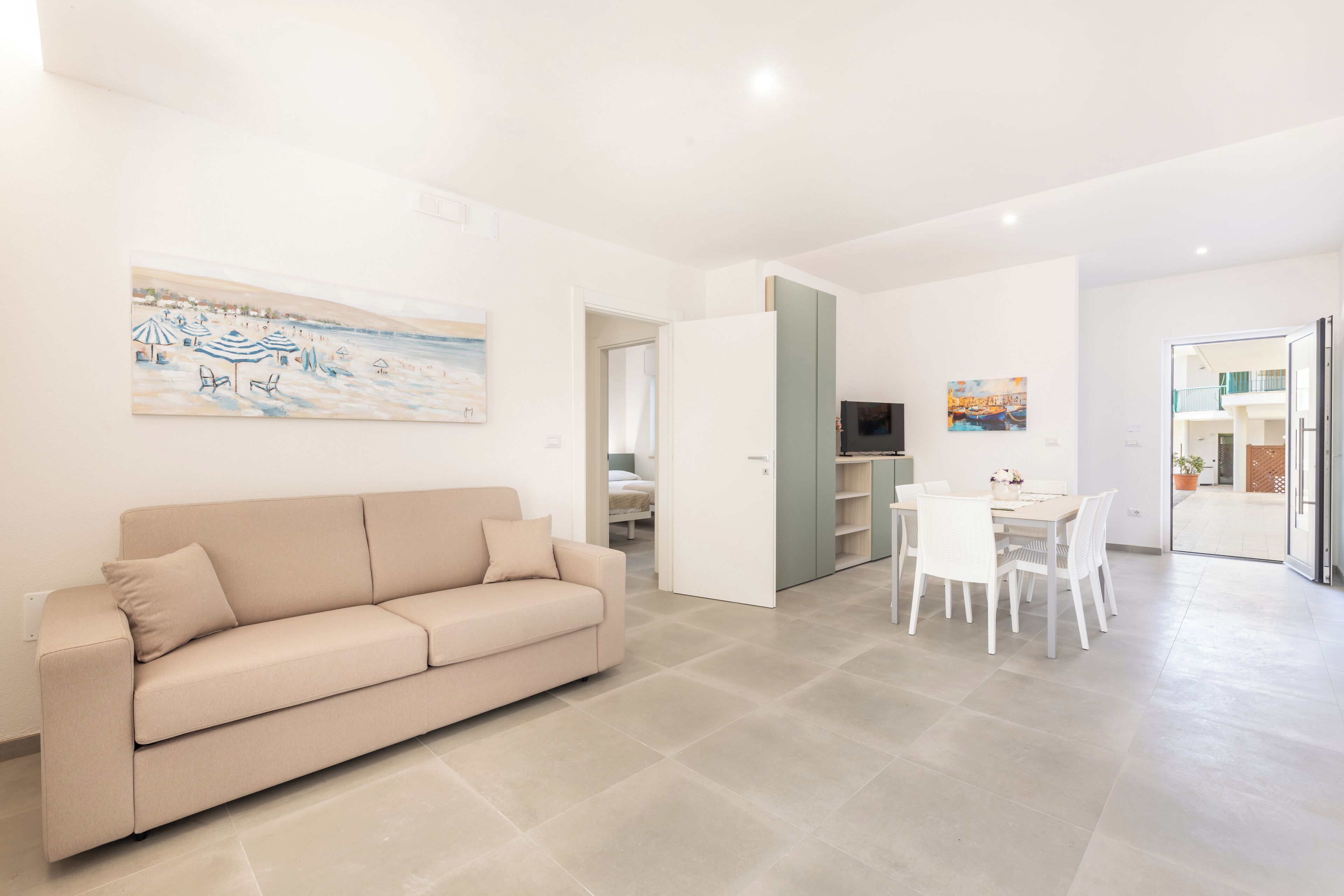 Uma sala de estar moderna com um sofá bege, uma mesa de jantar com cadeiras e uma cozinha visível por uma porta aberta.