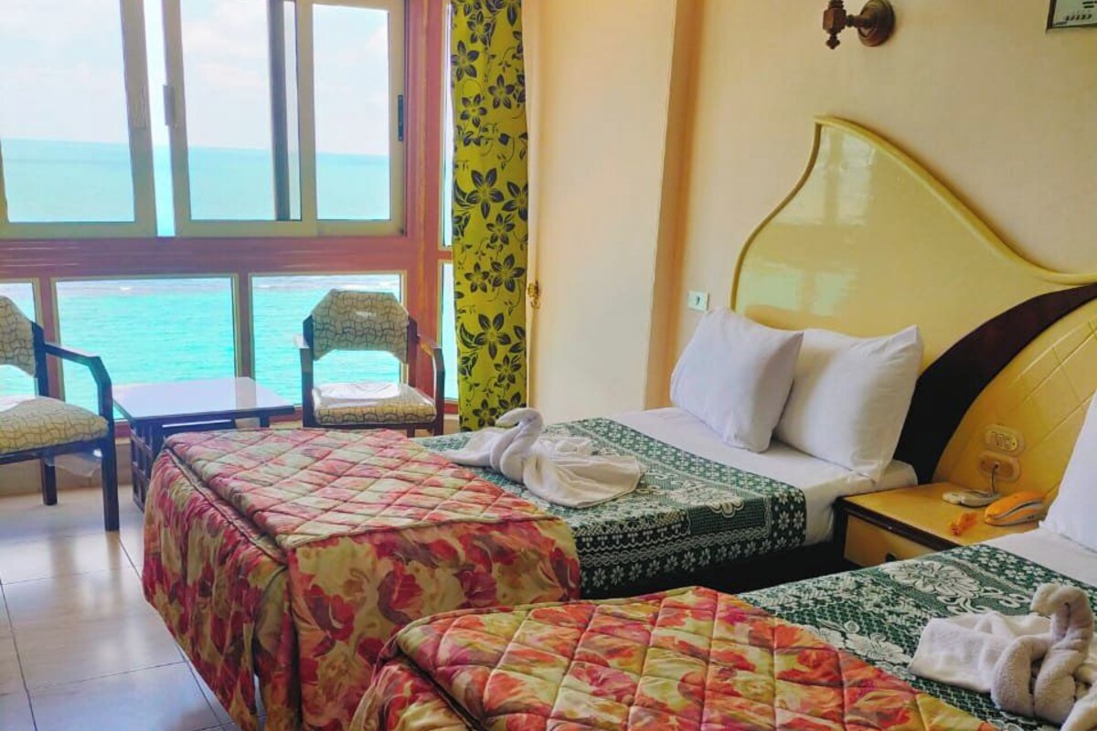 A hotel room with two beds, a view of the sea, and a balcony with chairs.