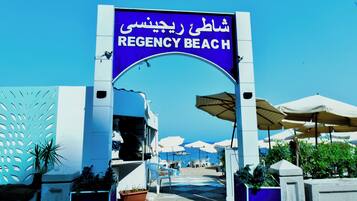 A sign for Regency Beach with a clear view of the beach and umbrellas in the background.
