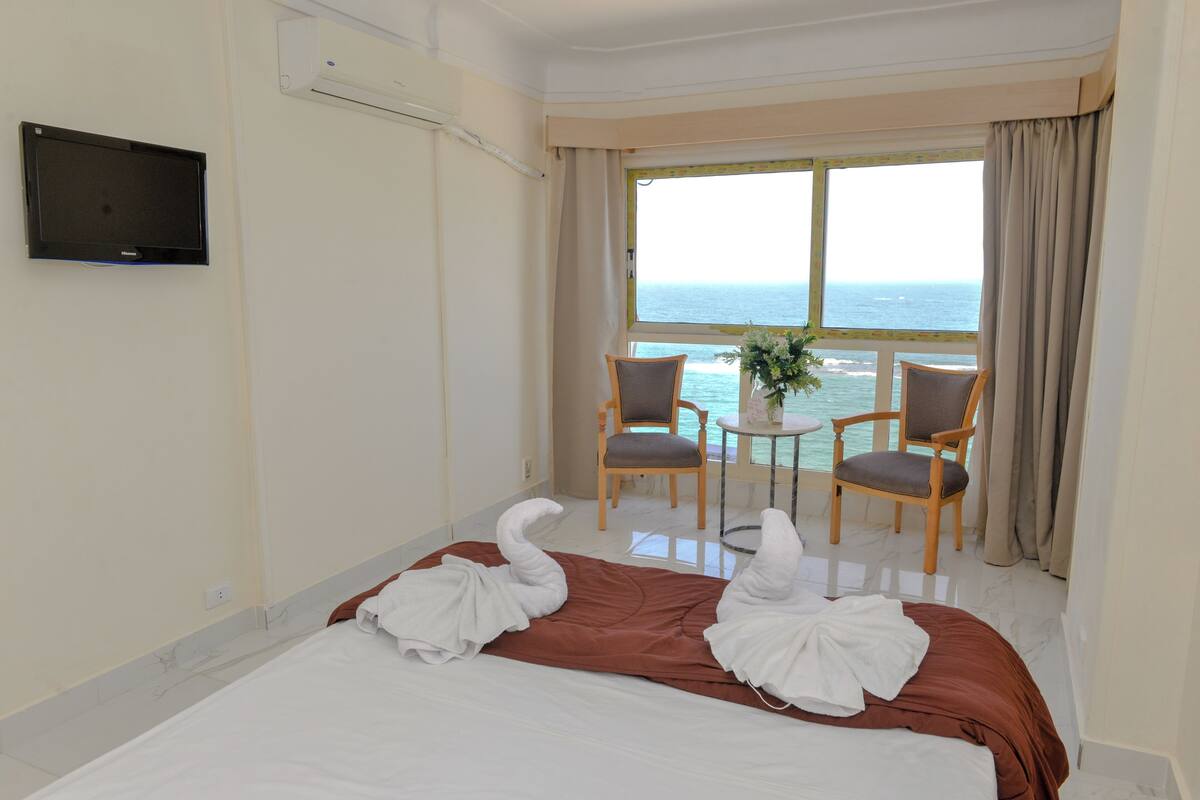 A hotel room with a bed, two chairs, a small table, and a TV on the wall.