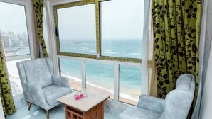 A balcony with two grey armchairs, a small wooden table, and a view of the ocean. - Regency Hotel Alexandria (Alexandria)