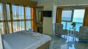 A hotel room with a bed, a TV, a small table with a plant, two armchairs, and a view of the sea. - Regency Hotel Alexandria (Alexandria)