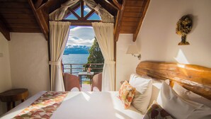 A bedroom with a large bed, a wooden headboard, and a view of a lake and mountains through a window.