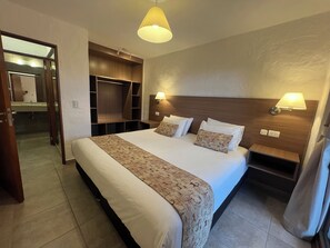 A hotel room with a large bed, bedside lamps, a wooden headboard, a built-in wardrobe, and a bathroom visible through an open door. - Costa Brava Apart Hotel (San Carlos de Bariloche)