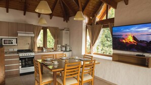 A cozy kitchen with wooden cabinets, a dining table set for four, and a large TV mounted on the wall displaying a scenic view.