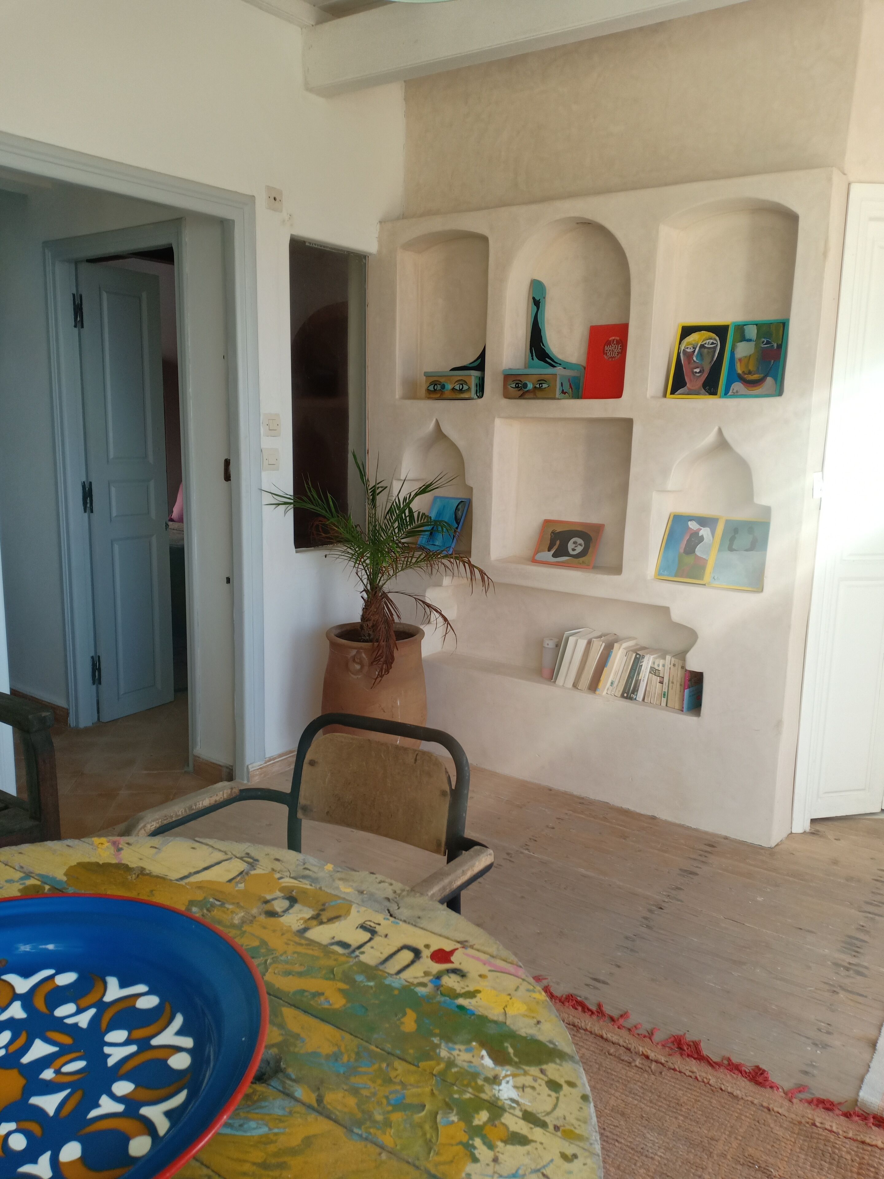 A room with a dining table, a potted plant, and a bookshelf with various items.