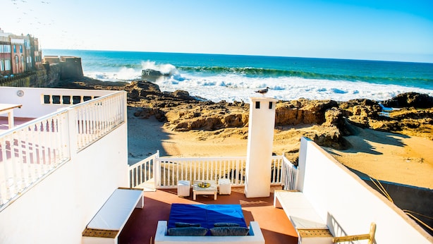 A balcony with a view of the ocean, a white railing, and a small table with chairs. - Dar Cherazade & Spa (Essaouira)