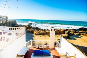 A balcony with a view of the ocean, a white railing, and a small table with chairs. - Dar Cherazade & Spa (Essaouira)