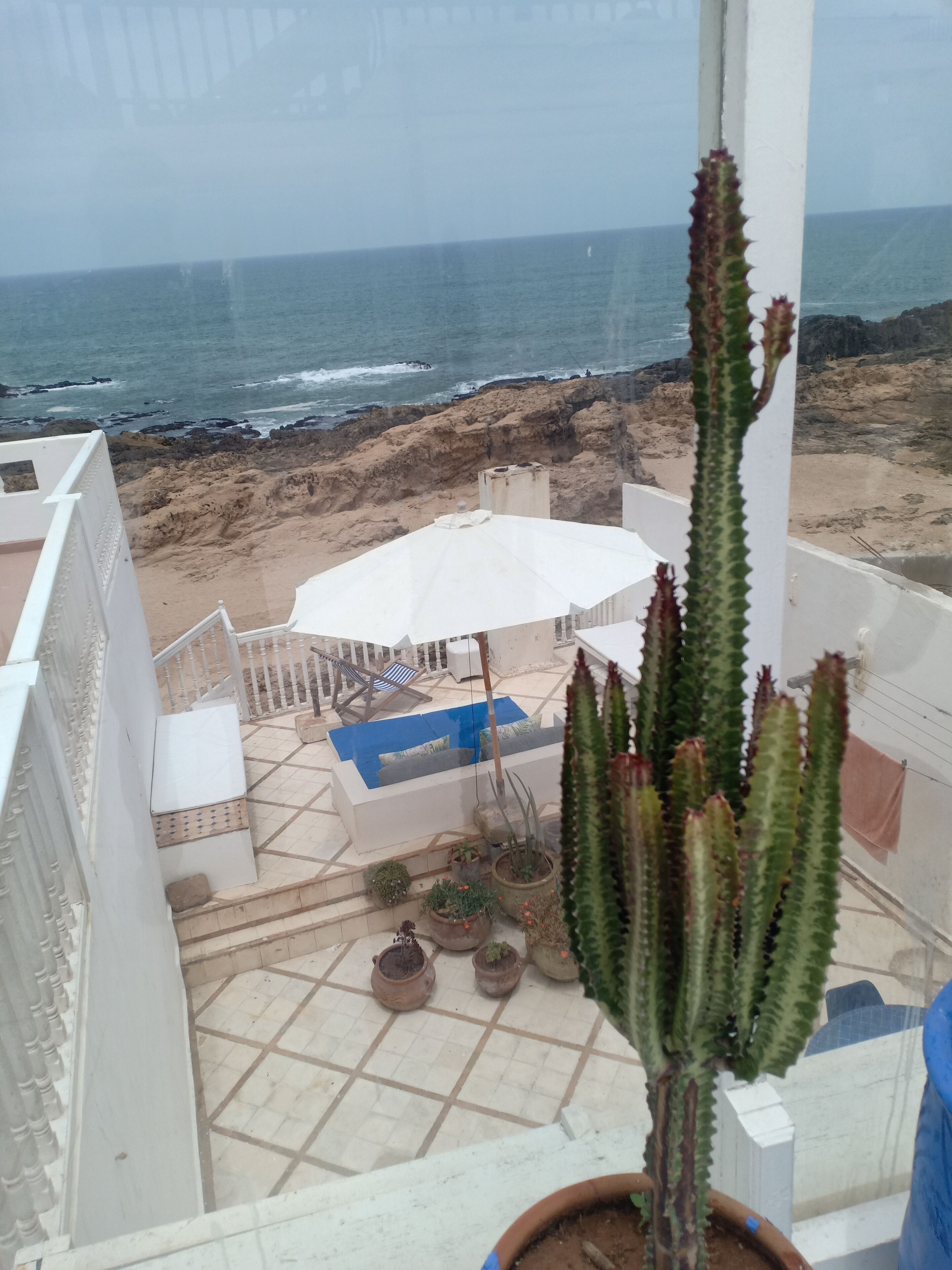A balcony with a view of the ocean, a white umbrella, and potted plants.