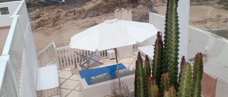 A balcony with a view of the ocean, a white umbrella, and potted plants.