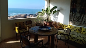 A room with a view of the ocean, a round table with chairs, a potted plant, and a tapestry on the wall. - Dar Cherazade & Spa (Essaouira)