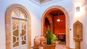 An interior courtyard with a large terracotta pot, arched doorways, and a stone fountain. - Dar Cherazade & Spa (Essaouira)