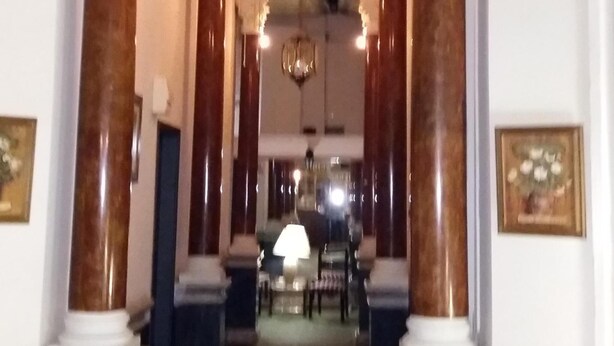 A corridor with marble columns, a chandelier, and framed artwork on the walls. - Hotel Uruguay (Montevideo)