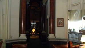 A dimly lit hallway with wooden columns, a ceiling fan, and a reception desk in the distance. - Hotel Uruguay (Montevideo)