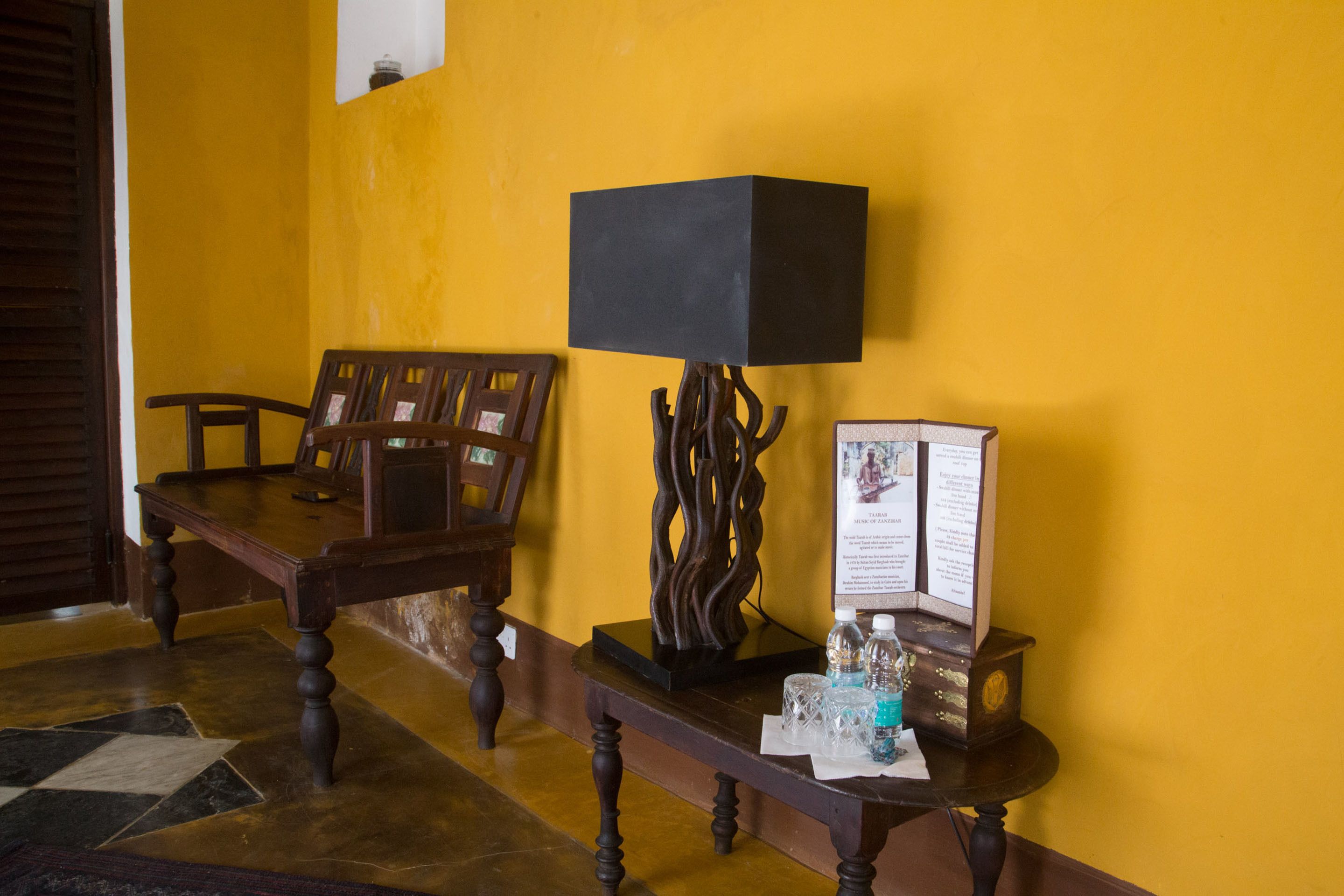 Una habitación con un banco de madera, una mesa con una lámpara negra y una pequeña vitrina con material informativo.