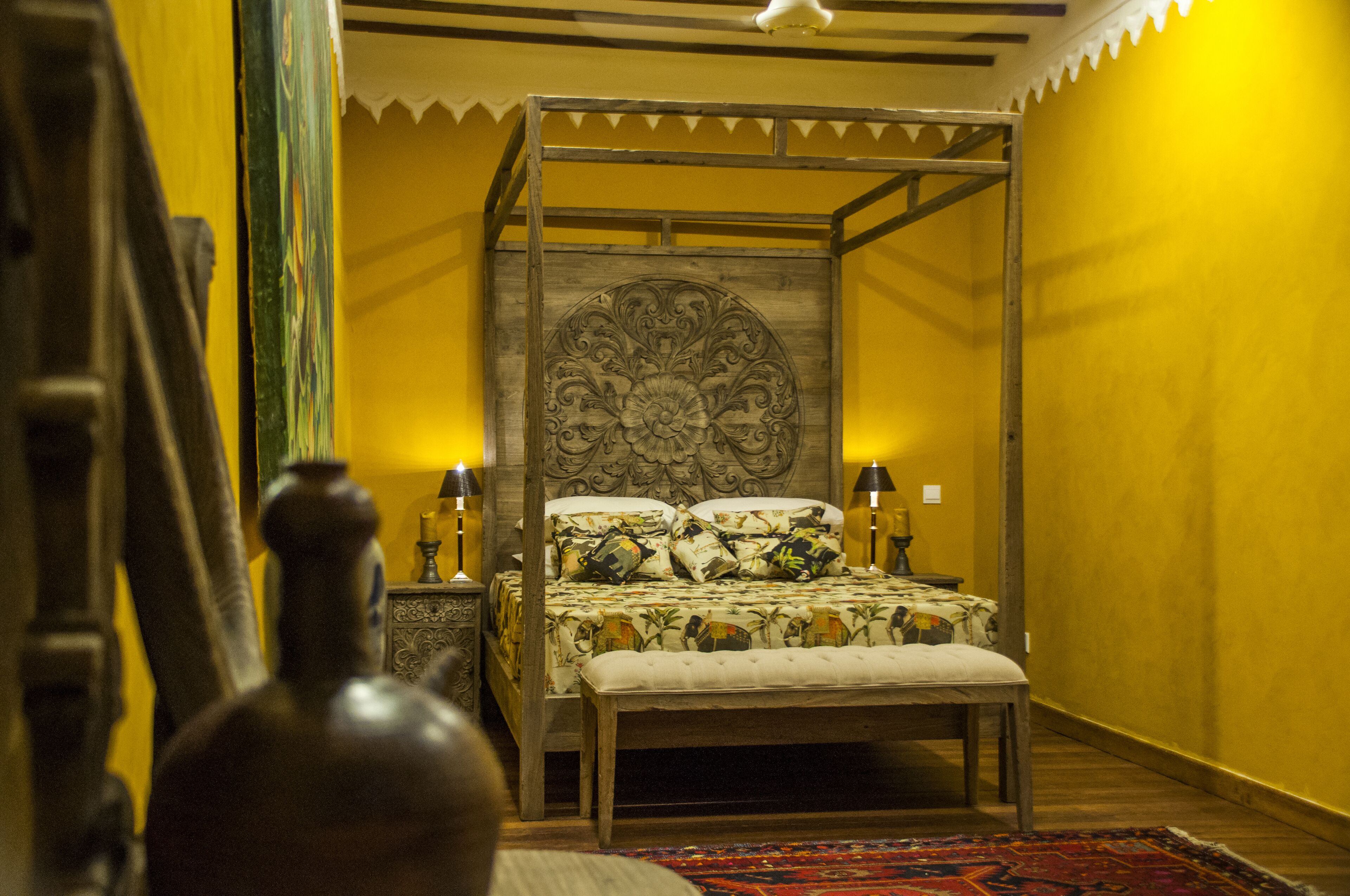 Un lit à baldaquin avec une tête de lit à motifs floraux, des lampes de chevet et un banc.