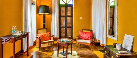 A room with a wooden floor, a round table, a sofa, a chair, a lamp, a mirror, and a dresser.