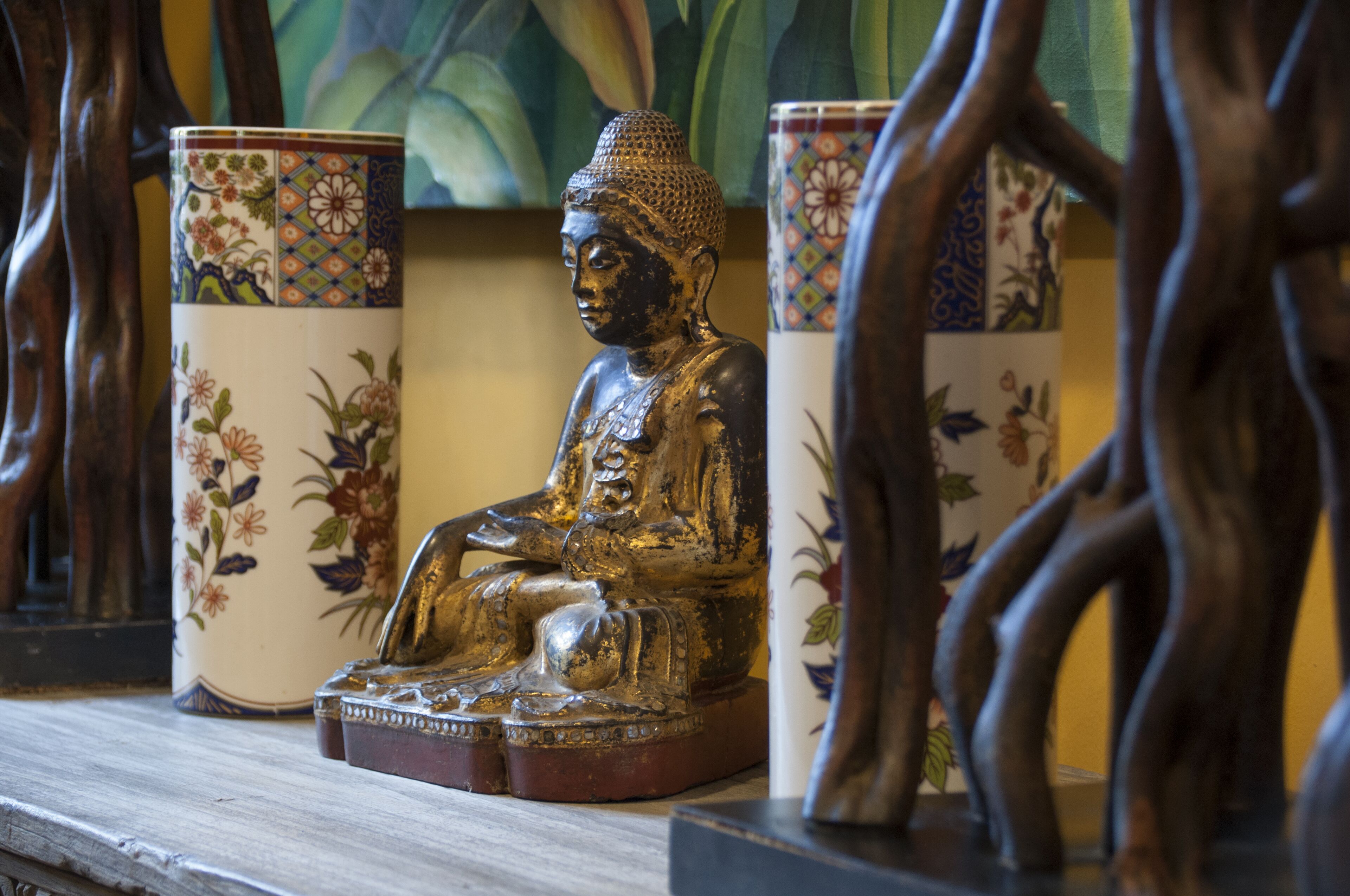 A Buddha statue on a wooden base, surrounded by two intricately designed vases.