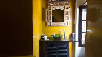 A bathroom with a yellow wall, a wooden cabinet, a green glass sink, and a mirror above it.