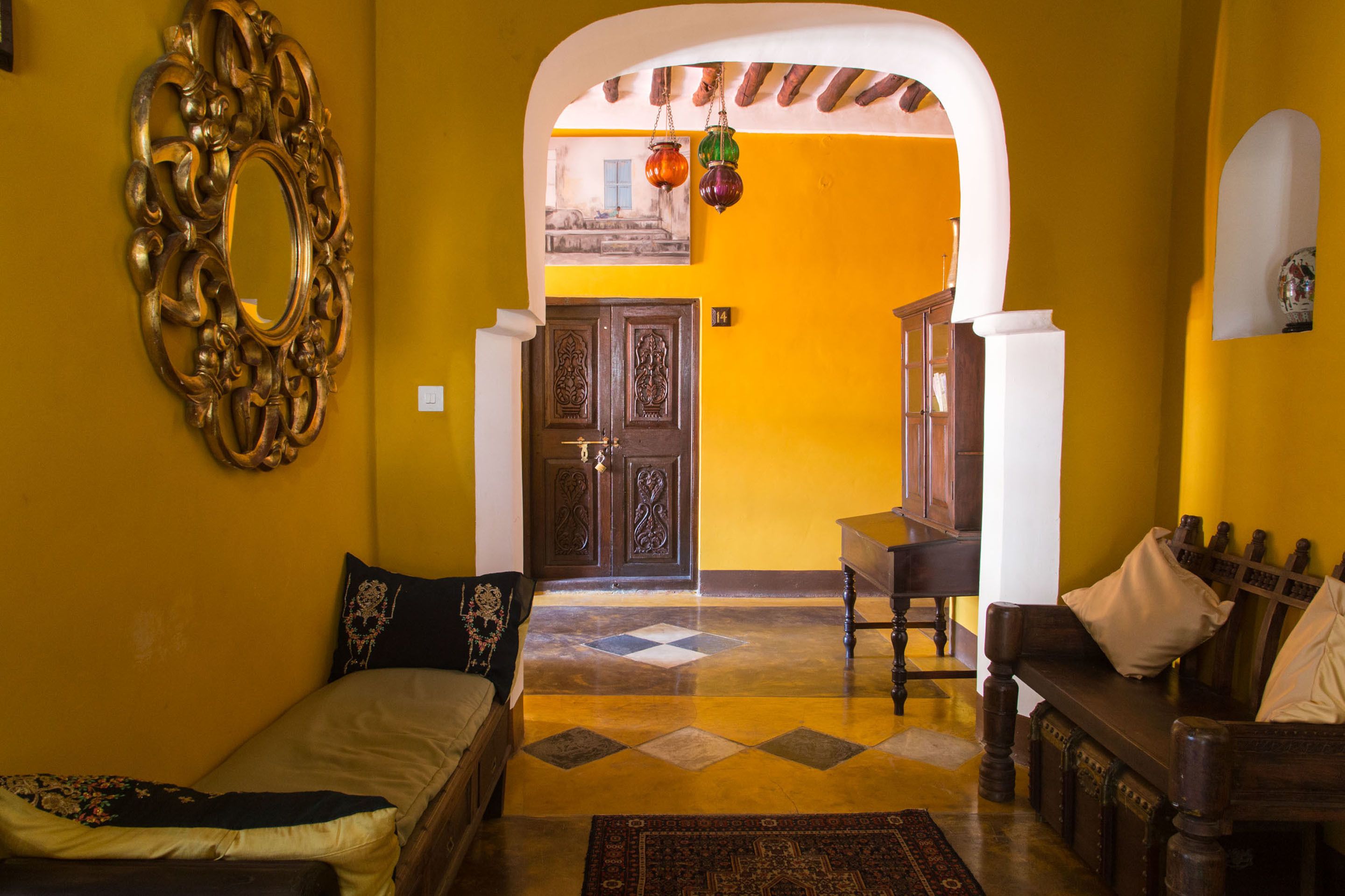 A room with a bed, a wooden bench, a mirror, and a door leading to another room.