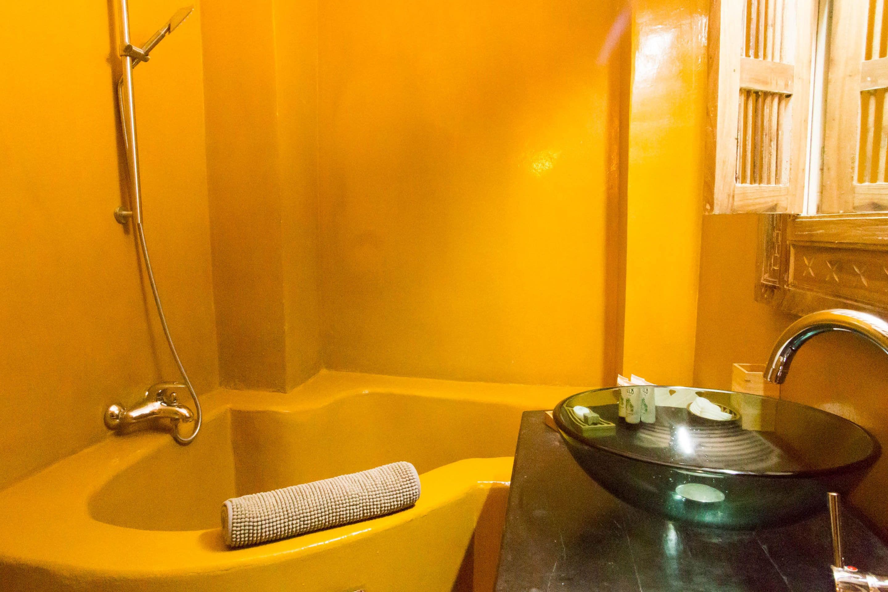 Un baño con un lavabo amarillo, una pila de cristal y una ducha.
