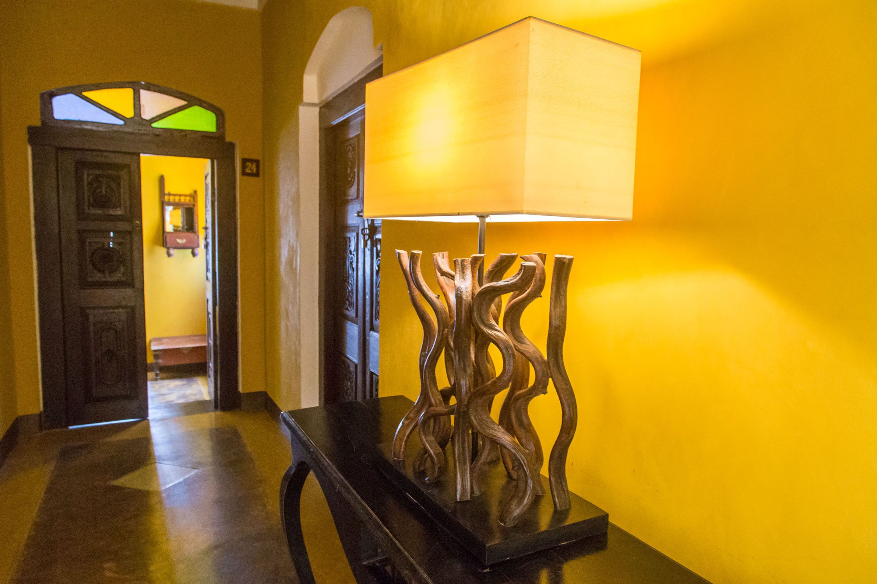 A hallway with a wooden floor, a lamp with a unique design, and a door with a stained glass window.