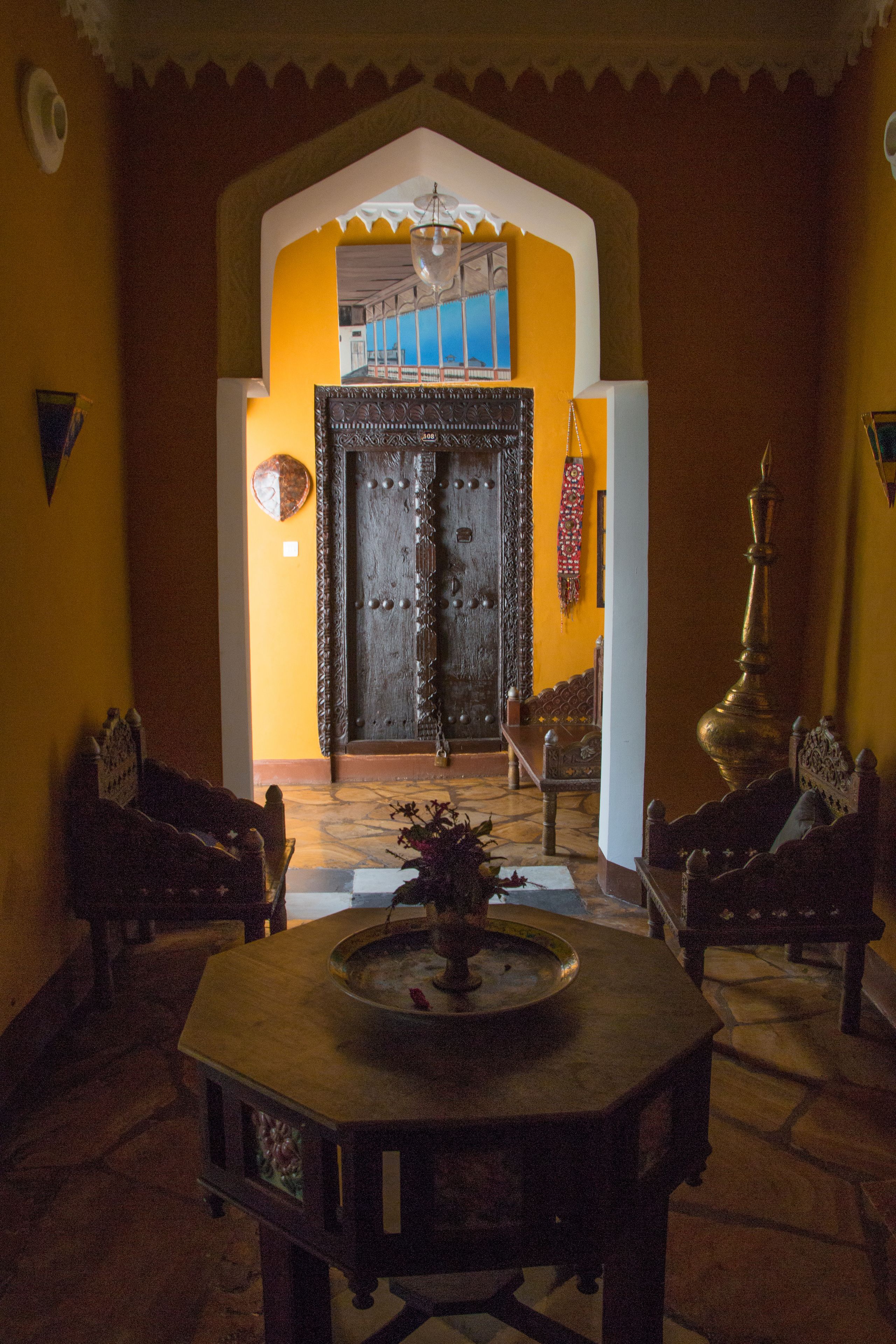 Um interior tradicional com uma grande porta de madeira, uma mesa central com um tabuleiro e duas cadeiras de madeira.