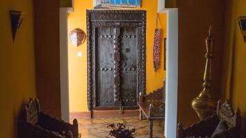 Um interior tradicional com uma grande porta de madeira, uma mesa central com um tabuleiro e duas cadeiras de madeira.