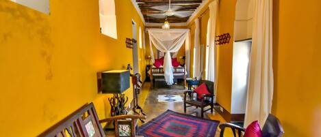 A hallway with a wooden ceiling, a patterned rug, and a chair with a red cushion.