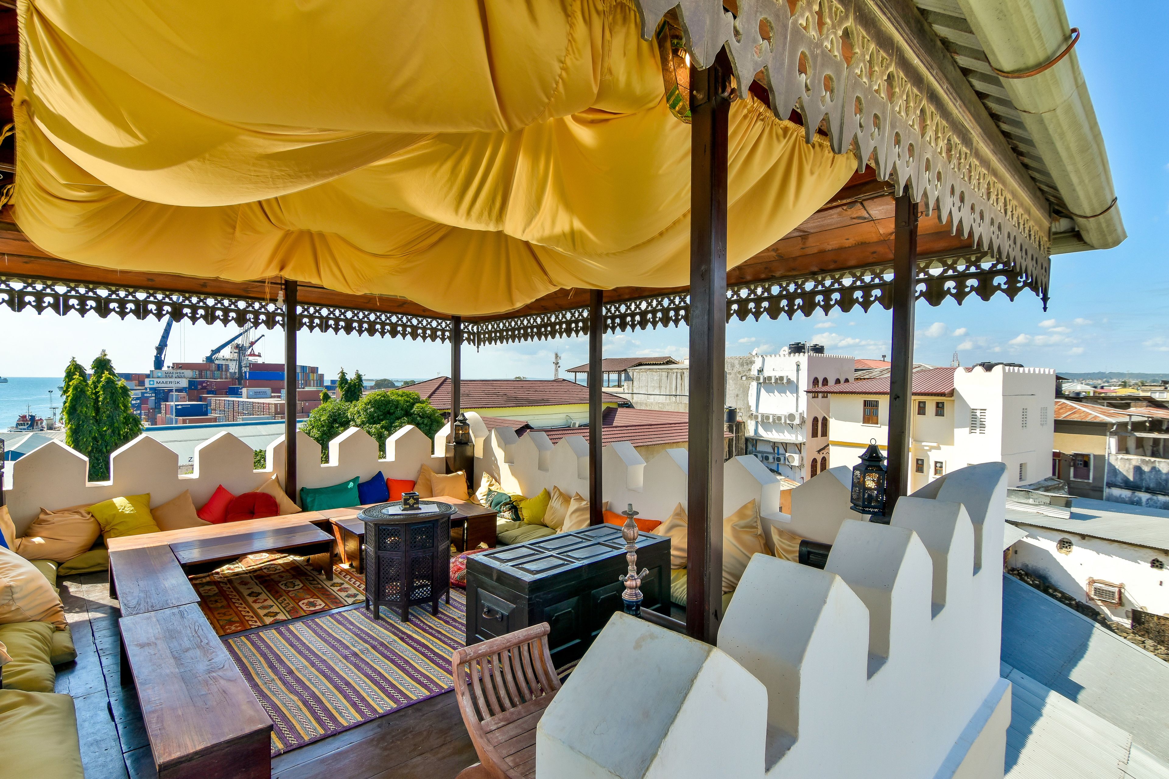 A covered outdoor seating area with a view of the sea and port.