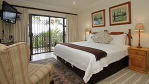 A hotel room with a bed, a chair, a nightstand, a TV, and a balcony with a view of palm trees. - Tesorino (Umhlanga)