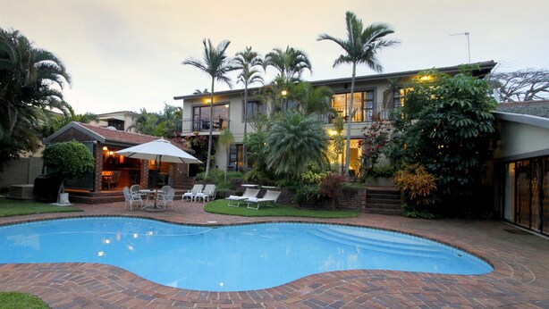 A swimming pool with a brick border, surrounded by a patio area with lounge chairs and a small table. - Tesorino (Umhlanga)