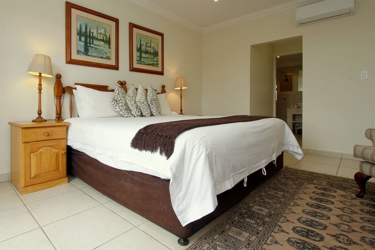 A neatly made bed with a brown headboard, two bedside lamps, and a patterned rug.