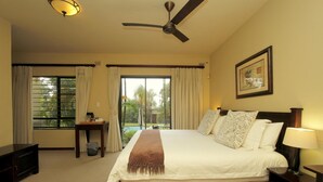 A hotel room with a large bed, a ceiling fan, a nightstand with a lamp, a small table with a lamp, and a window with curtains. - Tesorino (Umhlanga)
