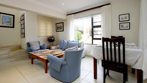 A living room with a sofa, a coffee table, a dining table with chairs, and a window with curtains. - Tesorino (Umhlanga)