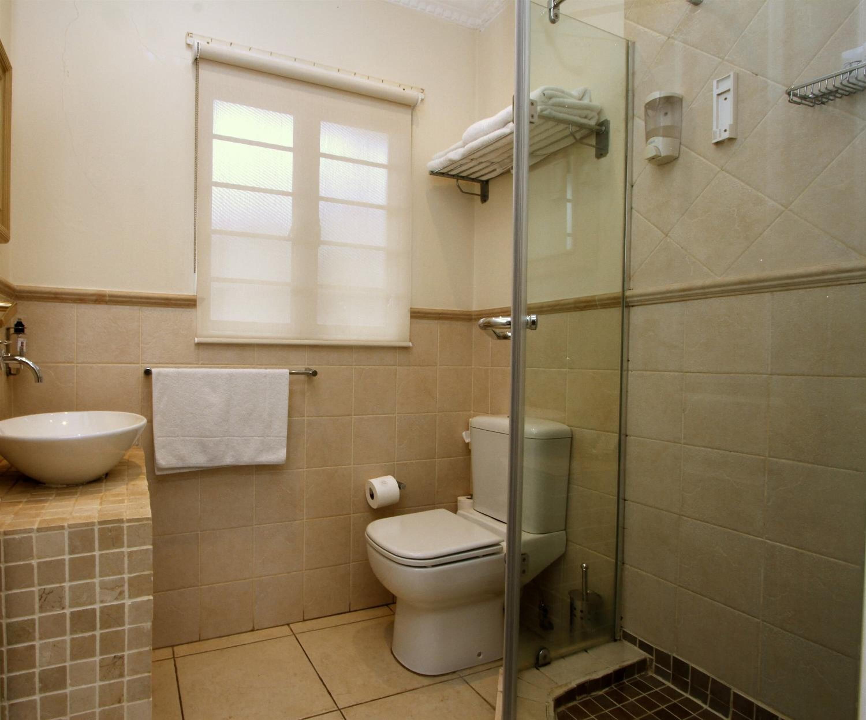A bathroom with a glass-enclosed shower, a toilet, a sink, and a window with blinds.