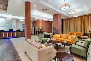 A hotel lobby with a reception desk, seating area, and a large window with curtains.