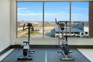A room with two stationary bikes, a large window with a view of buildings and a clear sky.