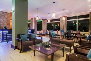 A modern hotel lobby with a reception desk, seating area, and large windows.