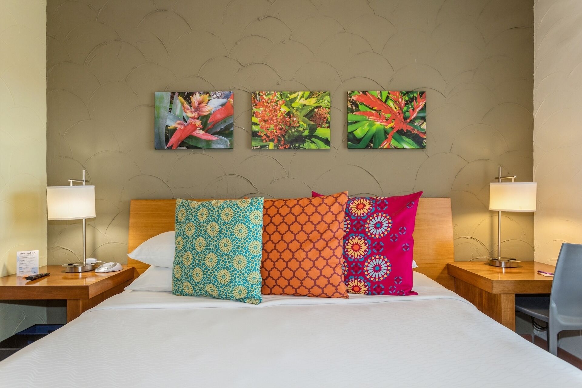 Ein Hotelzimmer mit einem Bett, zwei Nachttischen, zwei Lampen und drei Wandbildern mit Blumenmotiven.