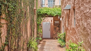 A narrow alleyway with brick flooring, a building with ivy-covered walls, and a door at the end.