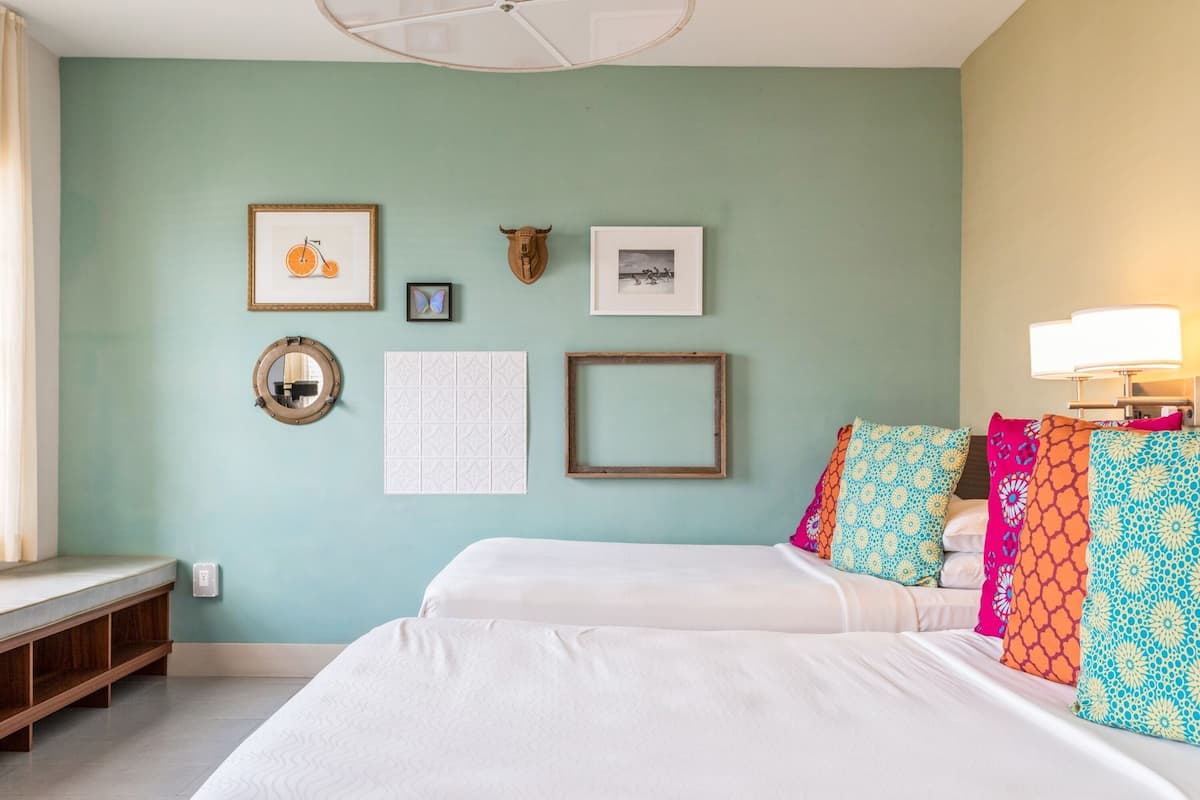 A bedroom with two beds, a wall clock, framed pictures, and a lamp.