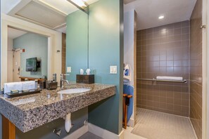 A bathroom with a granite countertop, sink, and a shower area with a towel rack.