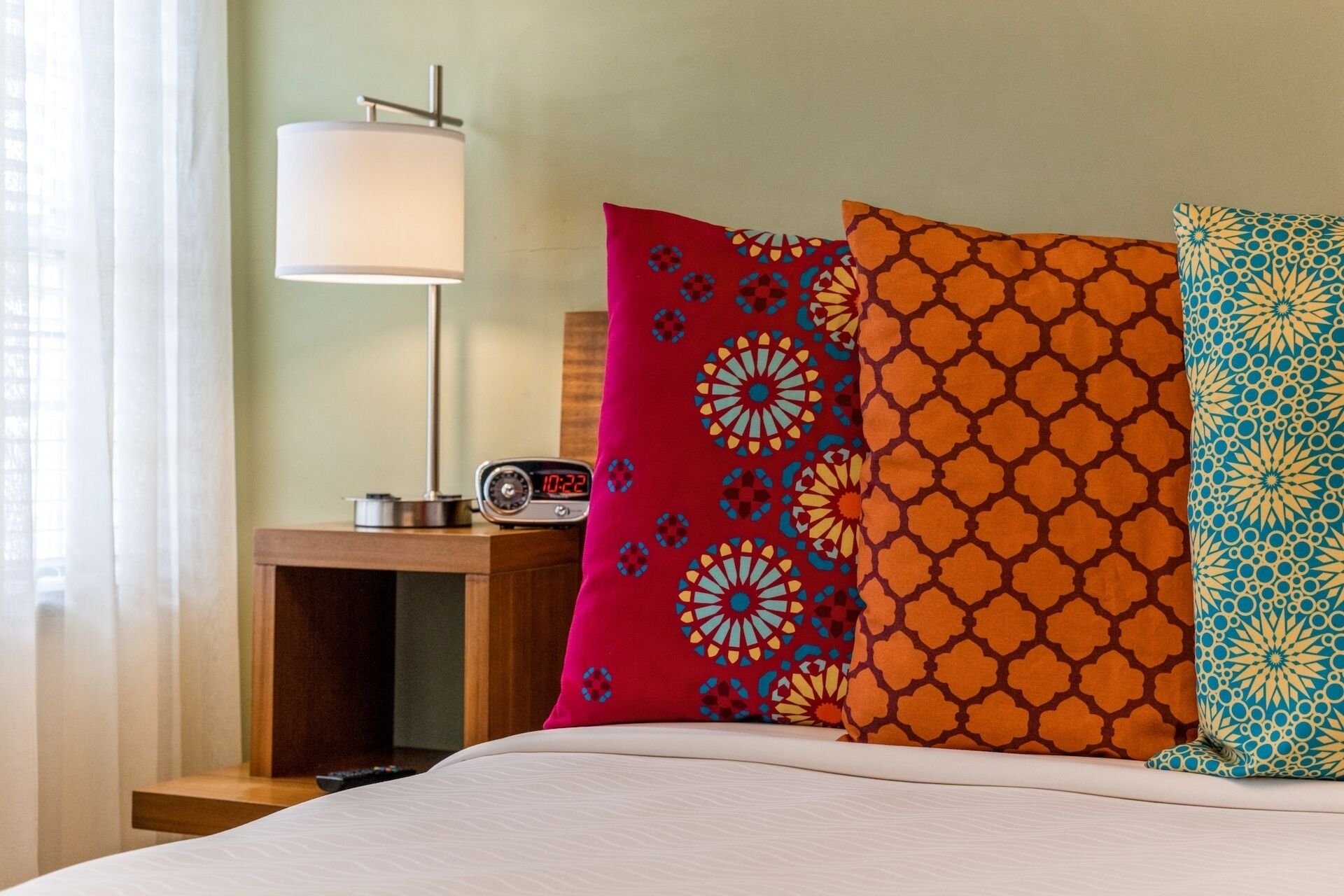 A hotel room with a bed, a bedside table with a lamp, and decorative pillows.