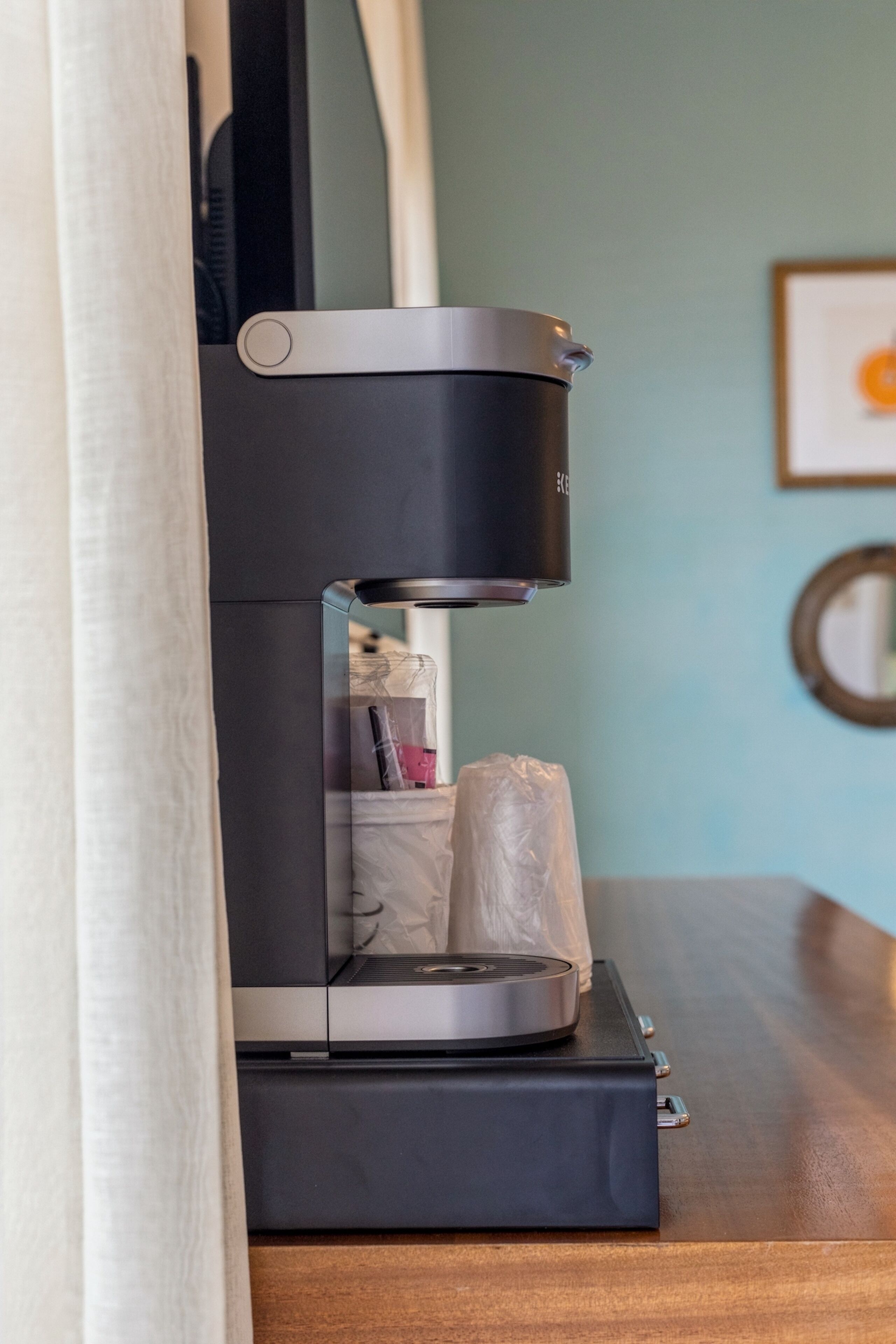 Uma máquina de café compacta sobre uma superfície de madeira, com um saco plástico e um pequeno objeto dentro.