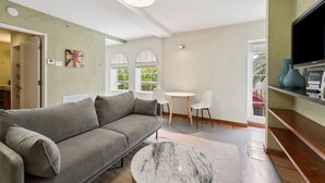 A modern living room with a grey sofa, a marble coffee table, white chairs, and a TV on a wooden shelf.