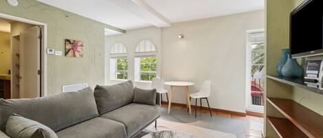 Ein modernes Wohnzimmer mit einem grauen Sofa, einem Marmortisch, weißen Stühlen und einem Fernseher auf einem Holzboden.