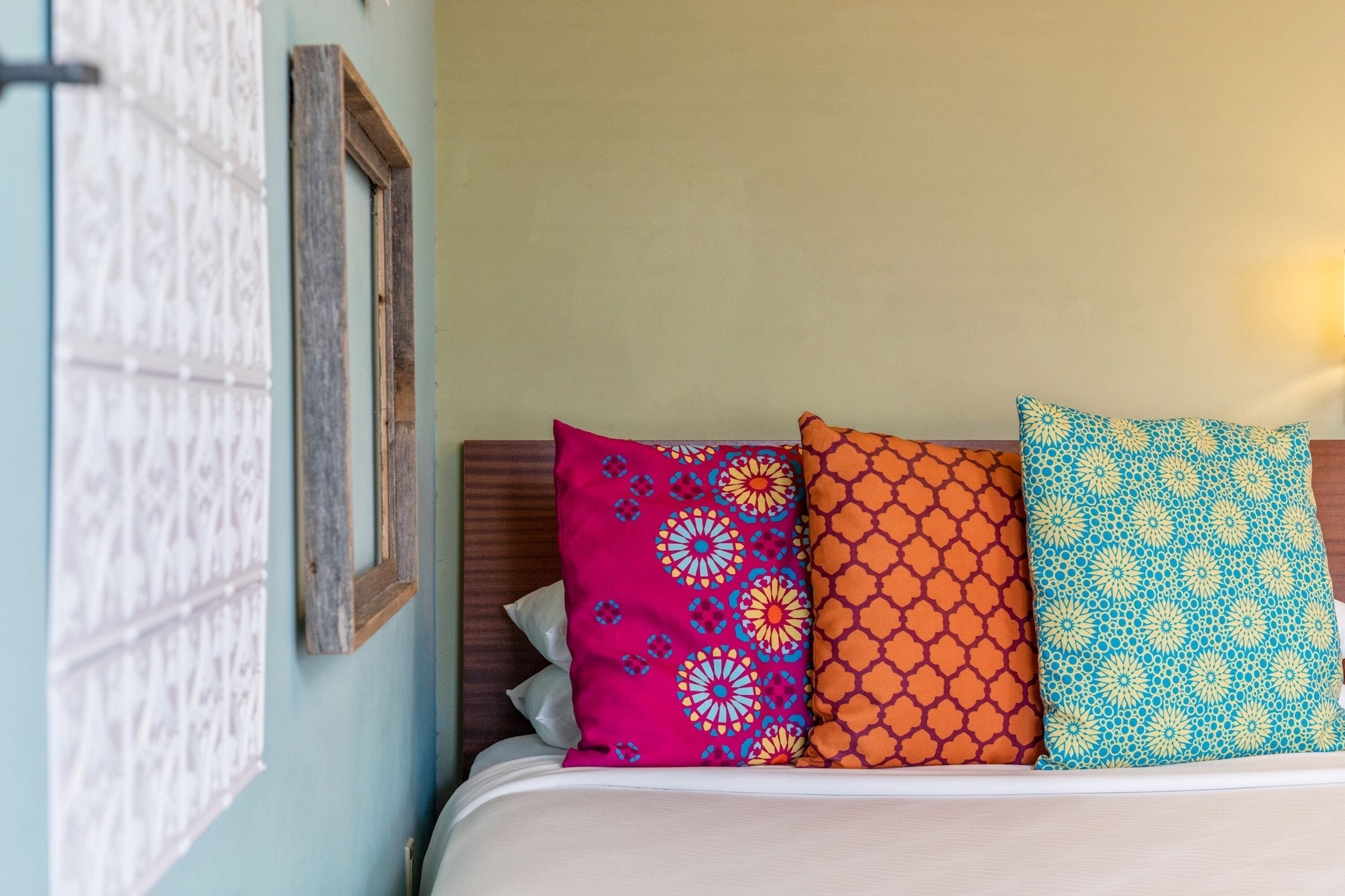 A bed with three pillows, a wooden headboard, and a wall with a patterned tapestry.