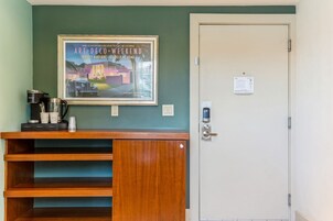A room with a framed poster on the wall, a coffee maker, and a door with a lock and a keycard reader.